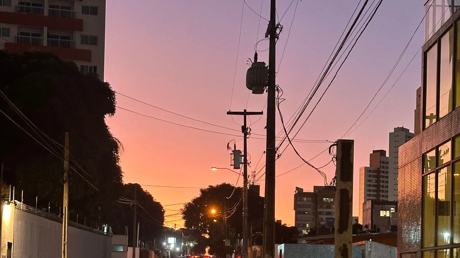 Rua urbana ao entardecer, com prédios residenciais ao fundo